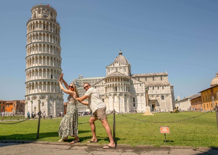 Visitors posing by the Tower of Pisa with Pisa Cathedral in Piazza dei Miracoli.