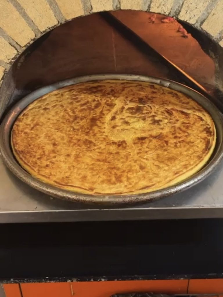 A whole cecina, one of the top Tuscan foods in Pisa, baking on a round tray in a wood-fired oven