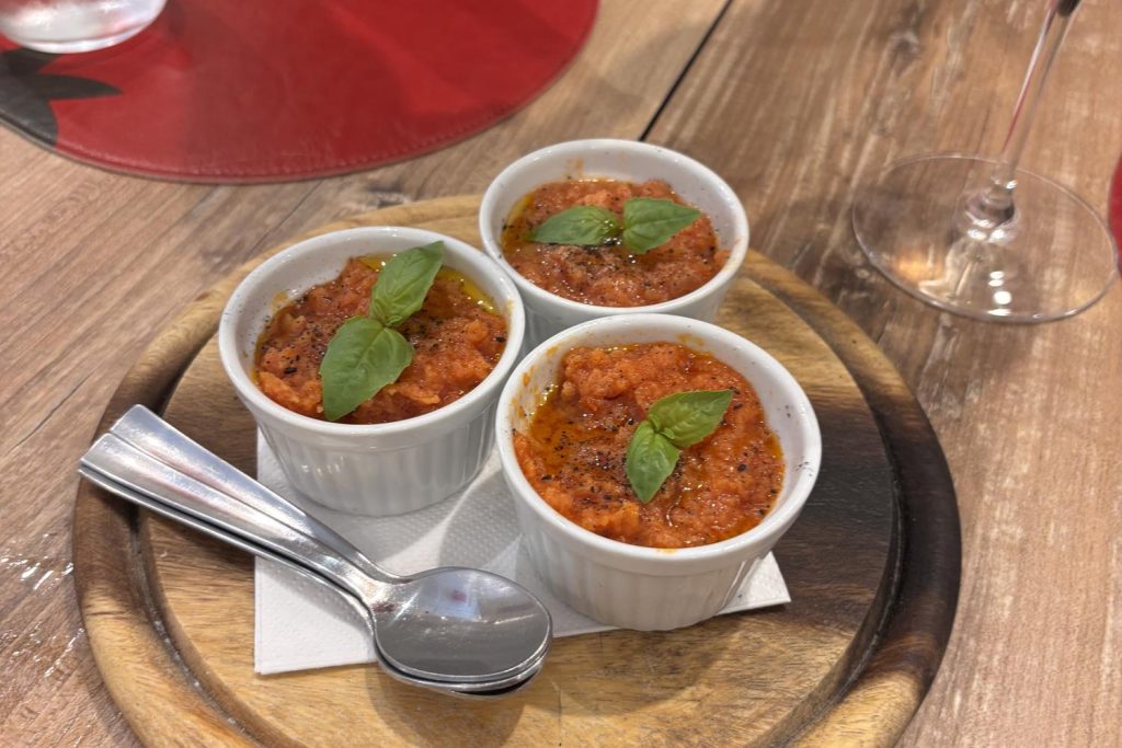 Three small cocottes of pappa al pomodoro, one of the top Tuscan foods in Pisa, with basil and olive oil on a wooden tray