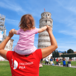 family-visiting-the-leaning-tower-of-pisa Parent holding a young child on their shoulders in front of the Leaning Tower of Pisa in Piazza dei Miracoli.